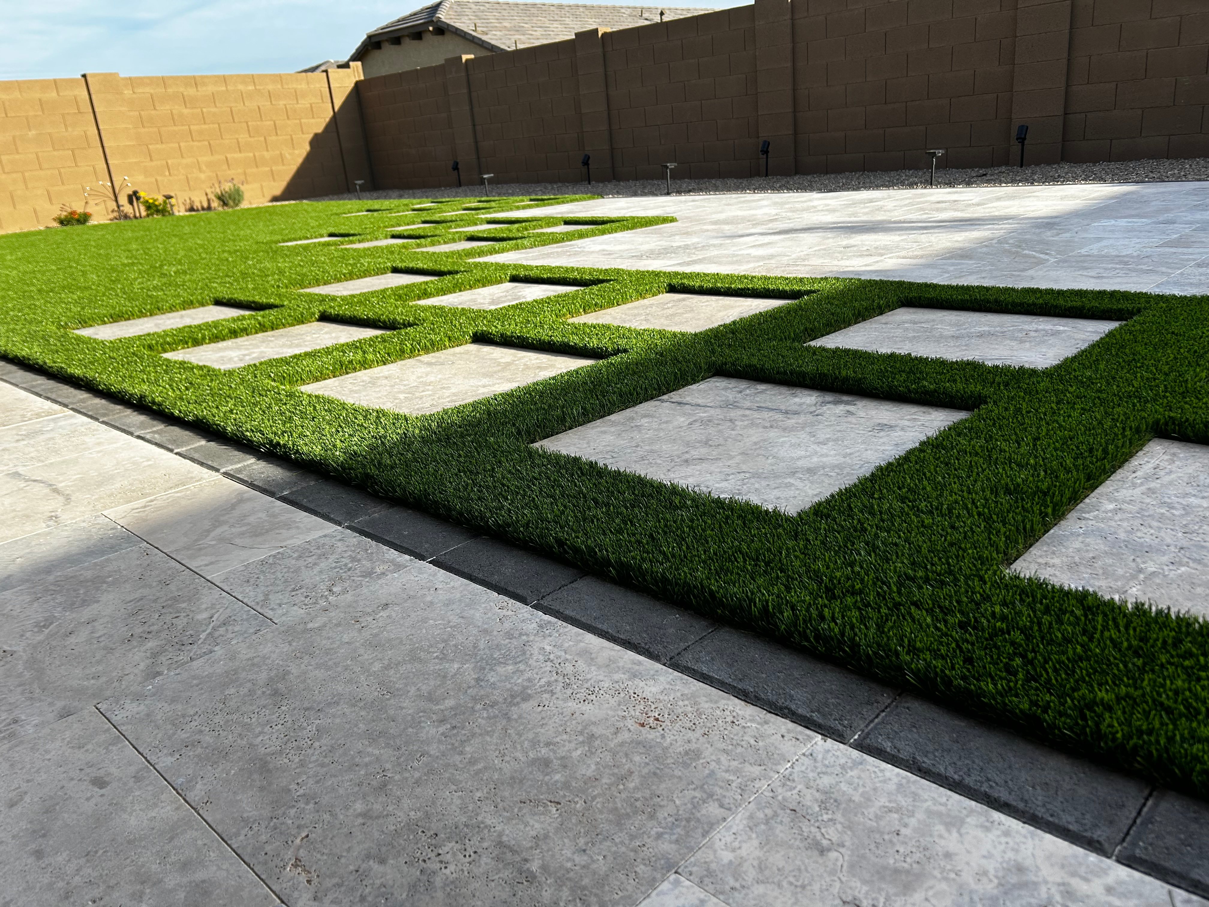 Artificial turf inlaid with large stone pavers in a geometric pattern beside a stamped patio